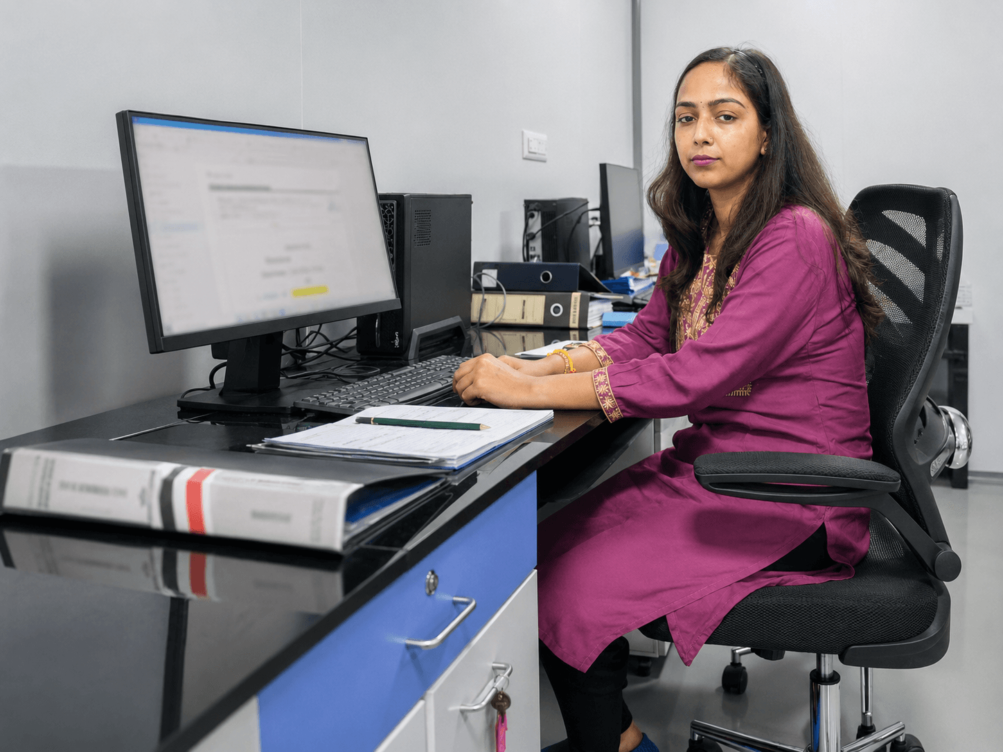 Saumya Dubey working at a QA desk with files and documentation.
